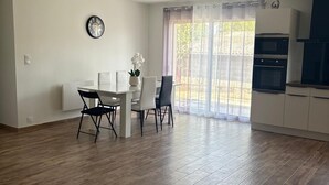 A spacious living area with a dining table, chairs, a clock on the wall, and a kitchen with an oven. - Large new house for 8 to 9 people, 105 m² (Ludiès)