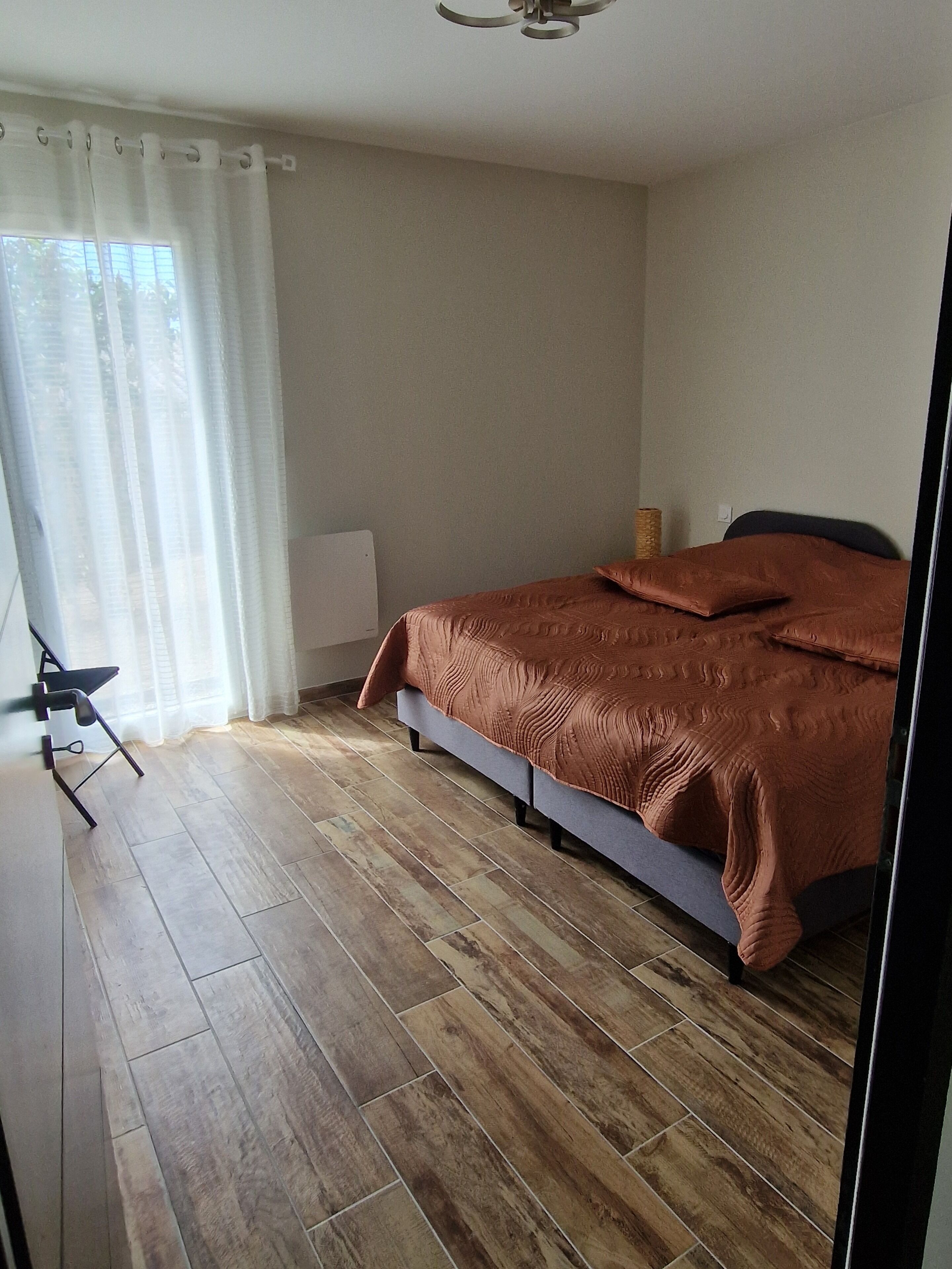 Een slaapkamer met een bed, een staande lamp, een radiator en een raam met gordijnen.