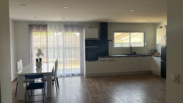A modern kitchen with white cabinets, a dining table with chairs, and a large window with a view of a tiled roof. - Large new house for 8 to 9 people, 105 m² (Ludiès)