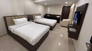 A hotel room with two beds, a desk, a chair, a TV, and a ceiling fan.