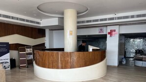 A reception area with a curved reception desk, a central pillar, a sign prohibiting outside food, and a lift sign.