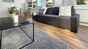 A modern living room with a dark grey sofa, a coffee table, and a dining area with chairs.