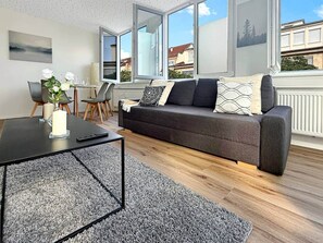 Ein modernes Wohnzimmer mit einem dunkelgrauen Sofa, einem Couchtisch und einem Essbereich mit Stühlen.