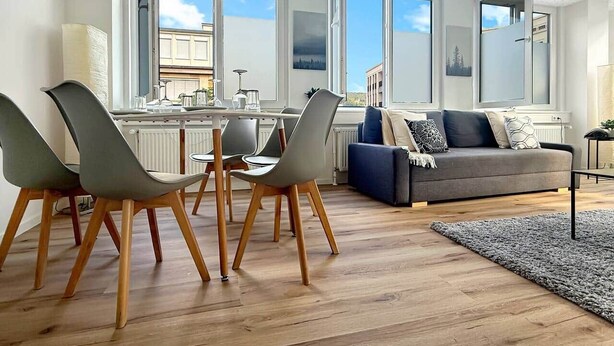 A modern living room with a dining area, large windows, and a grey sofa.