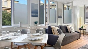 A modern living room with a dining area, large windows, and a grey sofa.