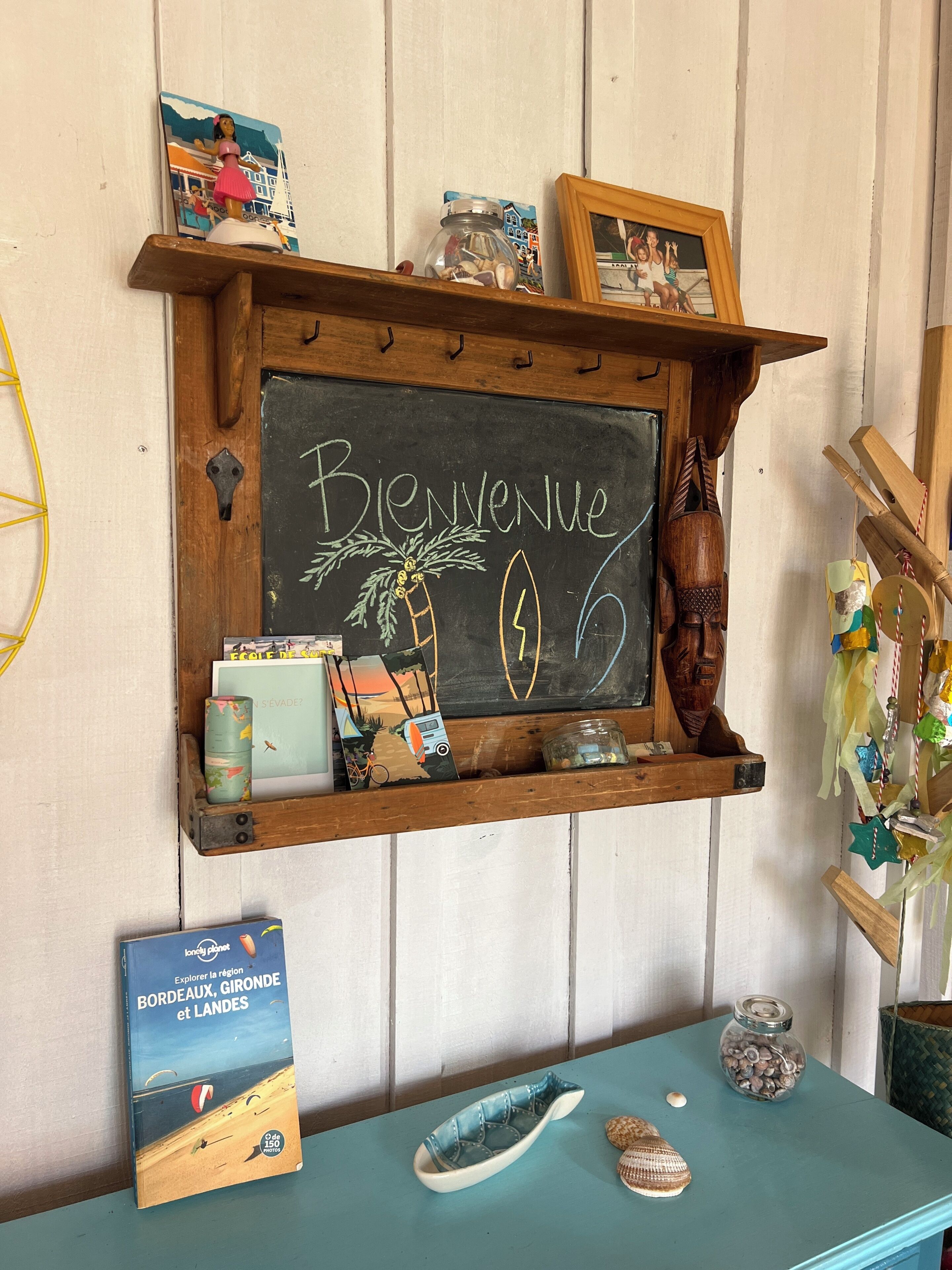 Une étagère en bois sur laquelle est posé un panneau noir avec l’inscription « Bienvenue », ainsi que divers objets, notamment des livres, une photo encadrée et des objets décoratifs.