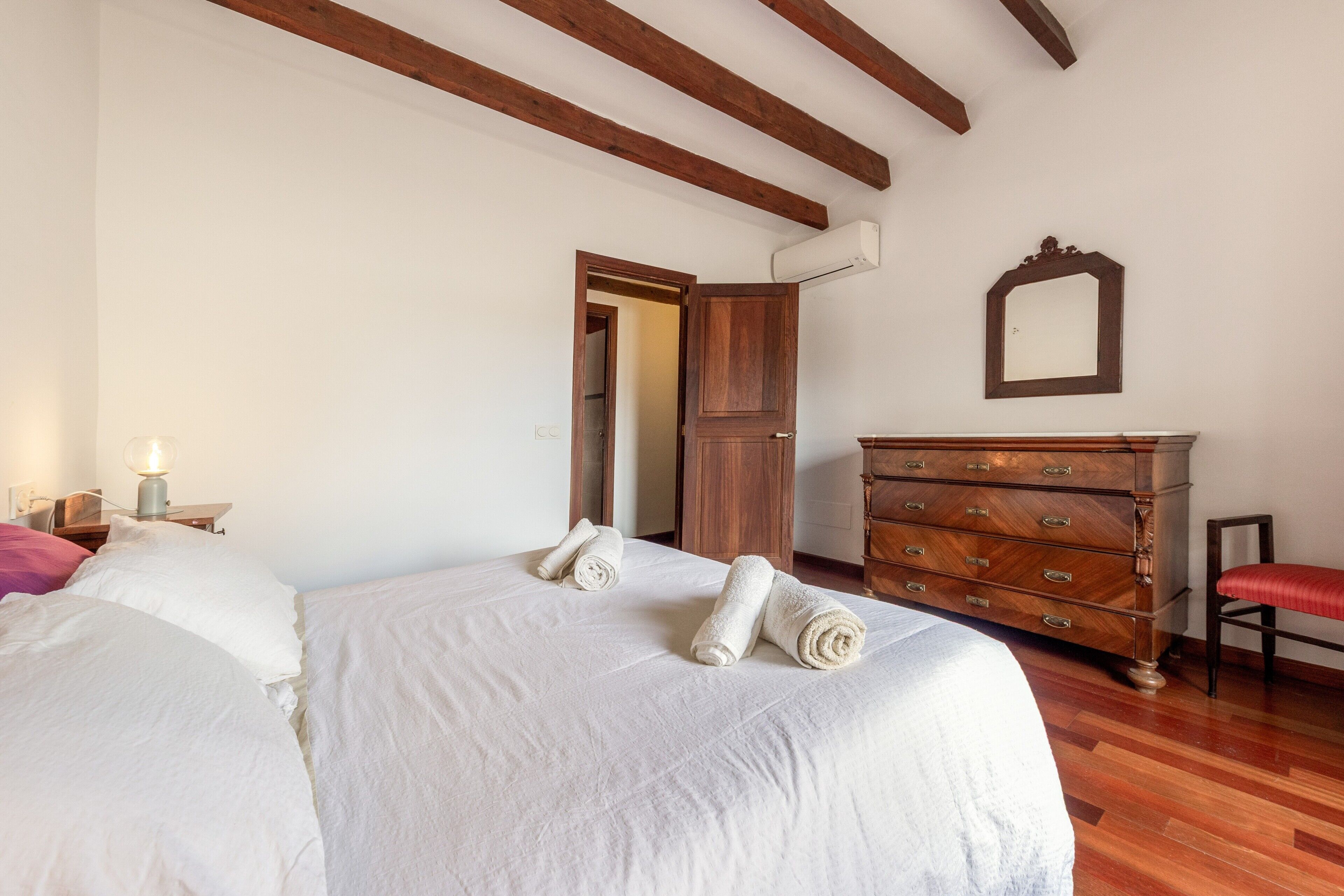 Un dormitorio con una cama, un aparador de madera, una silla y un espejo en la pared.