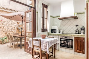 A compact kitchen with a dining area, stone walls, and a view through an open door.