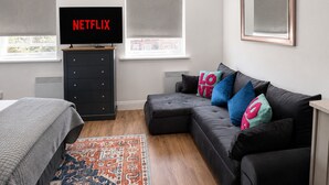 A modern bedroom with a black leather sofa, colorful pillows, a flat-screen TV, a dark dresser, and a patterned rug. - Shoreditch Studio Flat near Brick Lane & Liverpool St with Wi-Fi, Washer & Dryer (London)