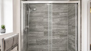 A walk-in shower with a glass door, grey patterned tiles, a handheld showerhead, and a towel rack with towels. - Shoreditch Studio Flat near Brick Lane & Liverpool St with Wi-Fi, Washer & Dryer (London)