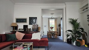 Ett vardagsrum med en röd soffa, ett soffbord, en matplats med bord och stolar samt en hall som leder till ett annat rum.