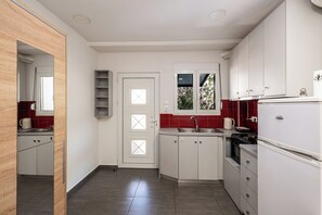Eine kleine Küche mit weißen Schränken, einer roten Fliesenspiegel und einem Fenster mit Aussicht, sowie ein Kühlschrank.