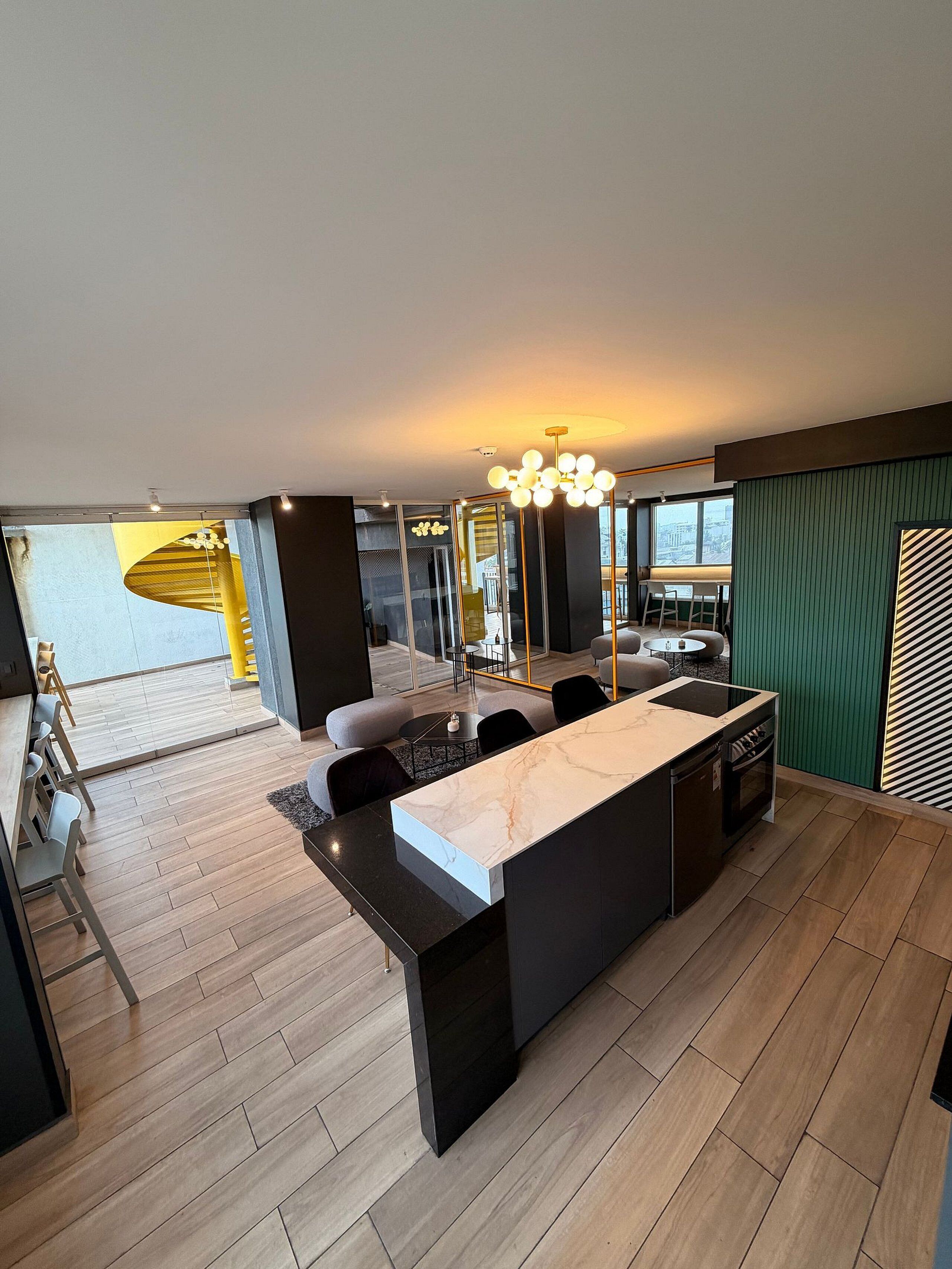 A modern kitchen with a marble countertop, wooden flooring, and a dining area with a yellow accent wall.