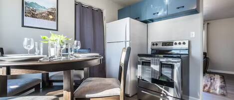 Une cuisine moderne dotée d’un four encastré, une table à manger mise avec des verres et des assiettes, et un tableau encadré accroché au mur.