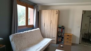 Una habitación con sofá, armario, estantería y ventana con cortinas.