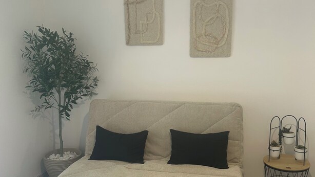 Una sala de estar con un sofá, dos cojines negros, una mesita, una planta en maceta y dos obras de arte en la pared.
