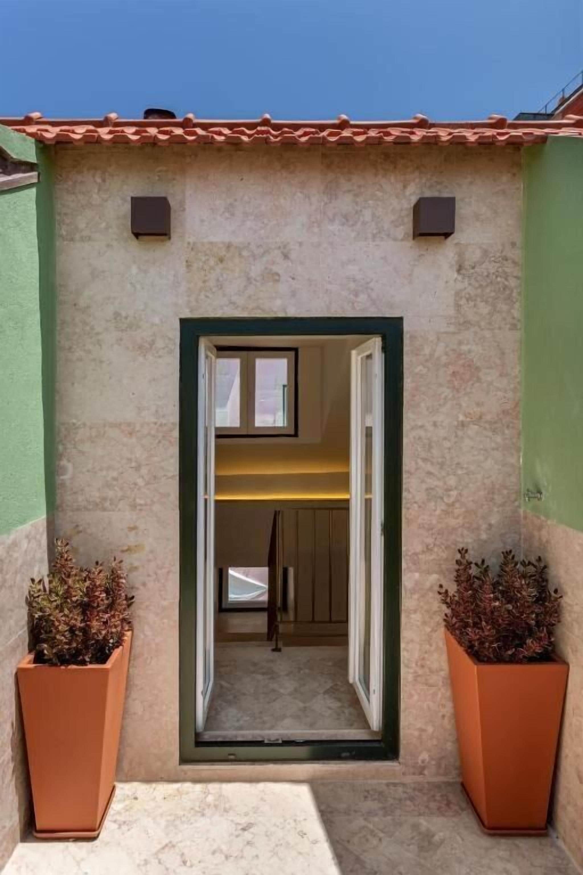 A building entrance with a green door, a small window, and two potted plants.