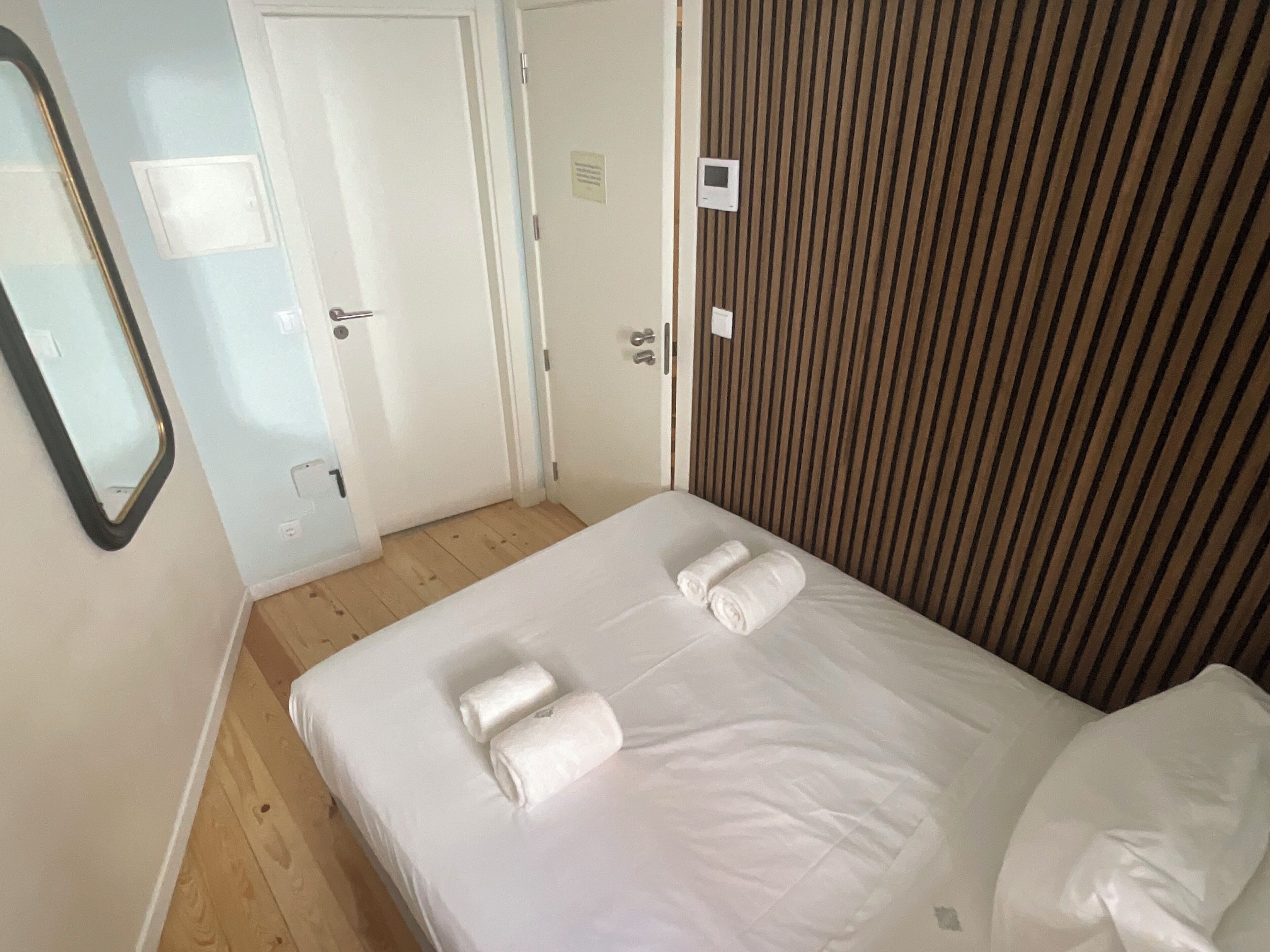 Une chambre d’hôtel avec un lit, deux serviettes, un plancher en bois, une porte blanche et un mur à rayures.