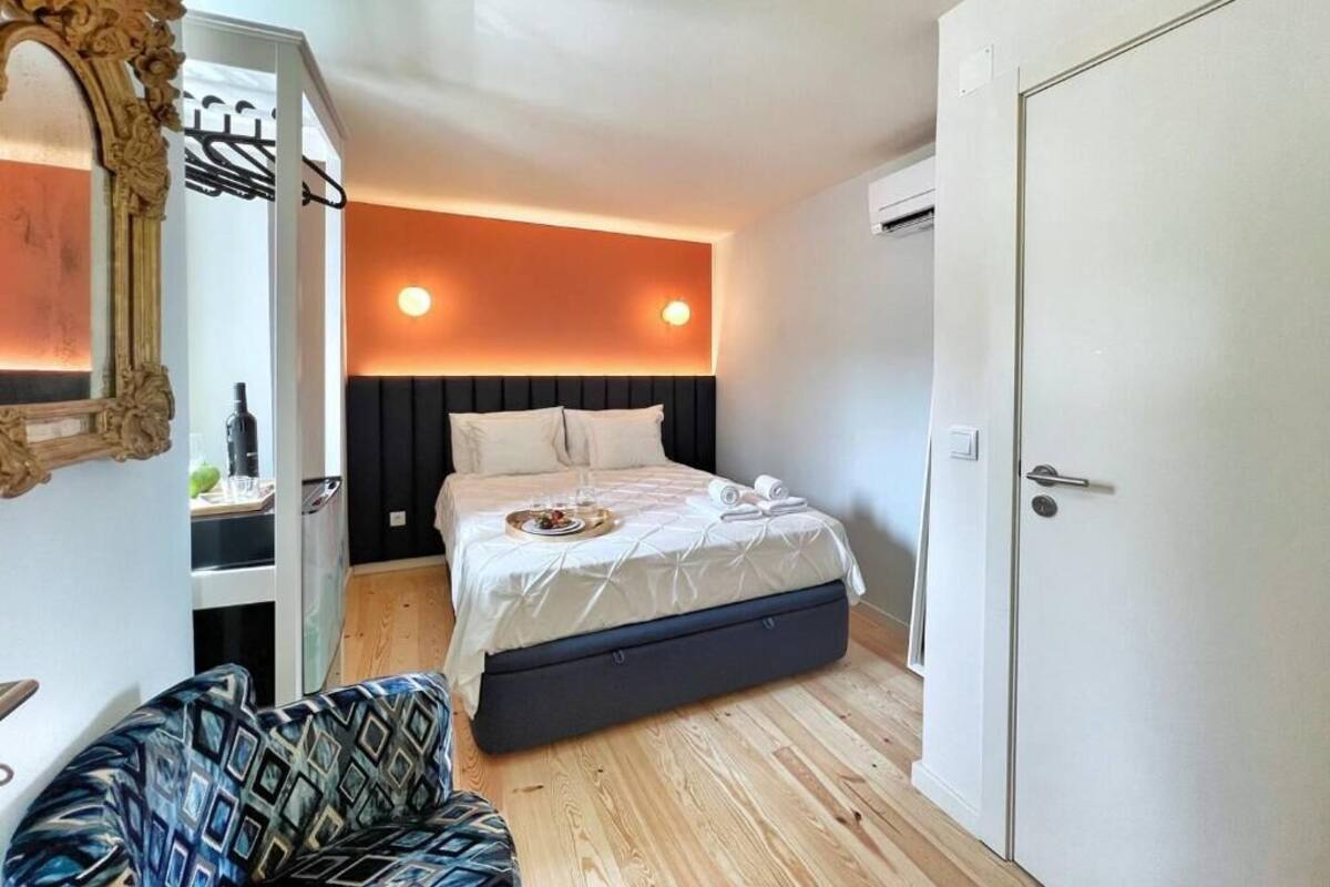 A bedroom with a bed, a wardrobe, a mirror, and a small seating area.
