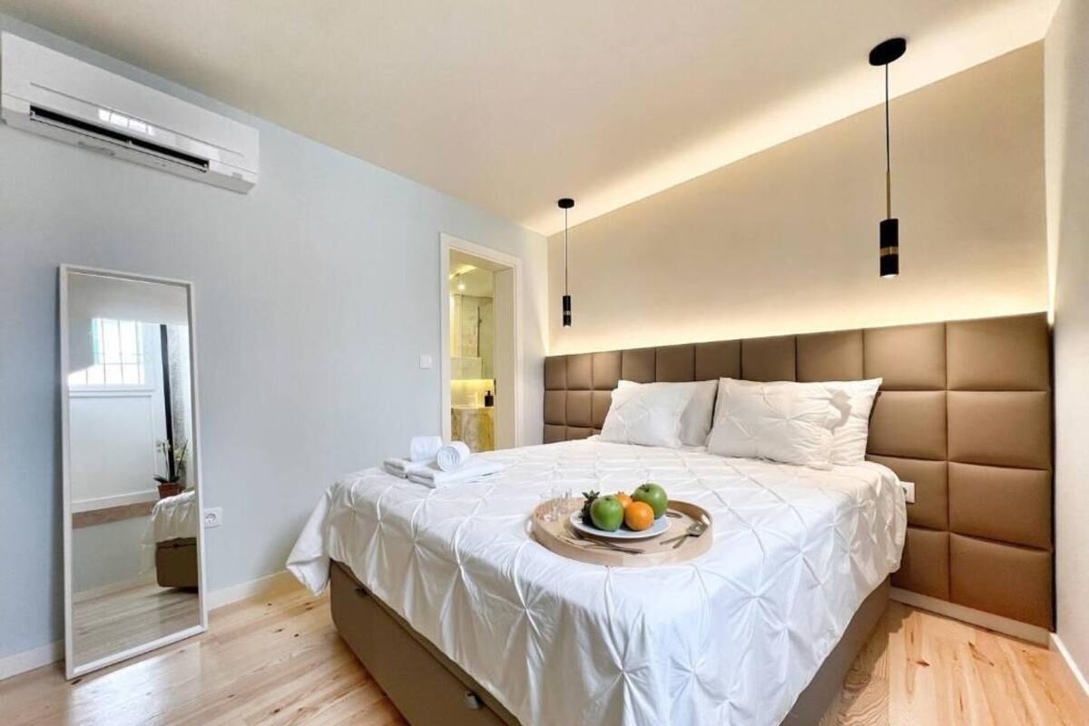 A bedroom with a bed, a bedside table, a mirror, and a wall-mounted air conditioner.