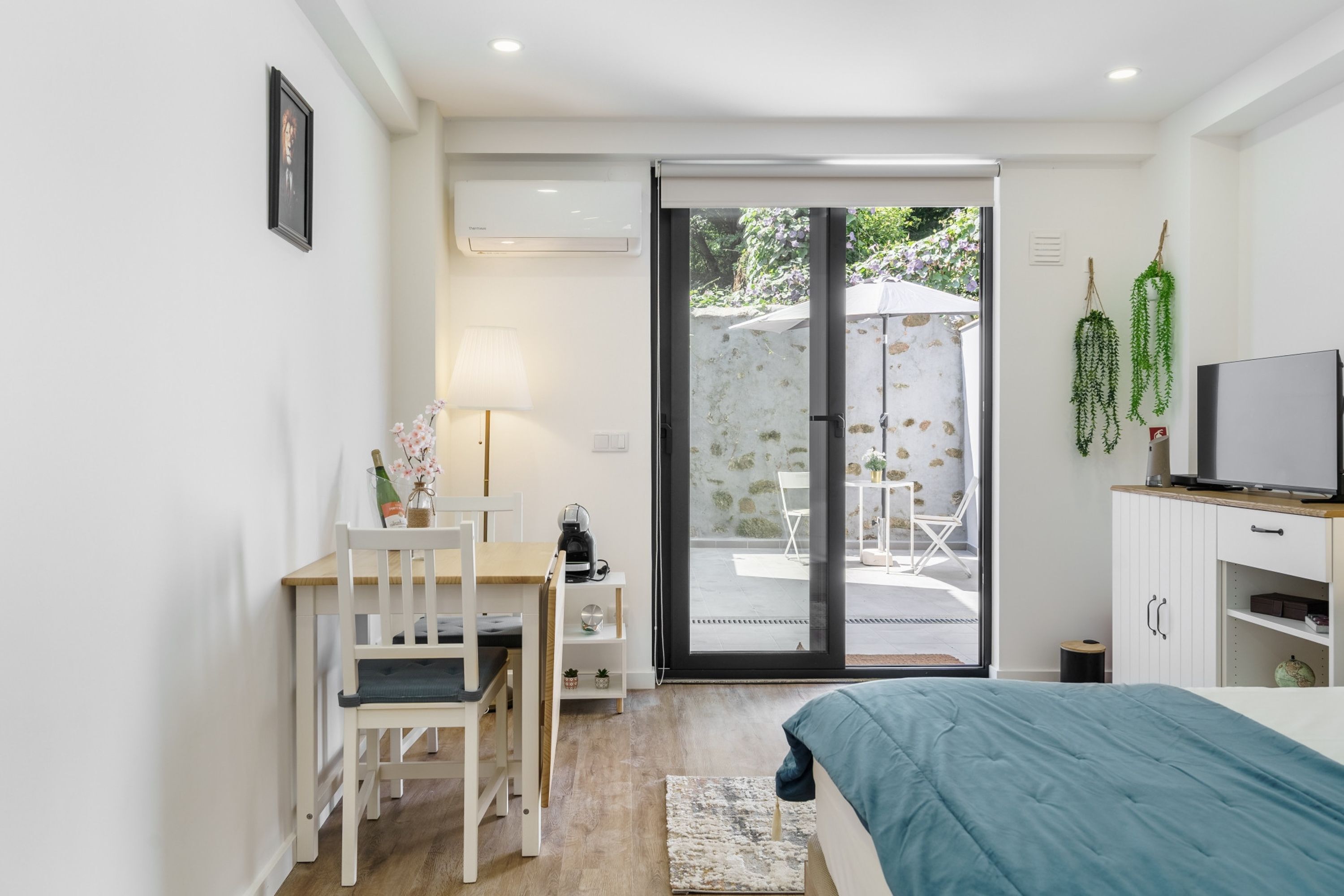 A bedroom with a bed, a desk with a chair, a television, and a sliding glass door leading to an outdoor area.