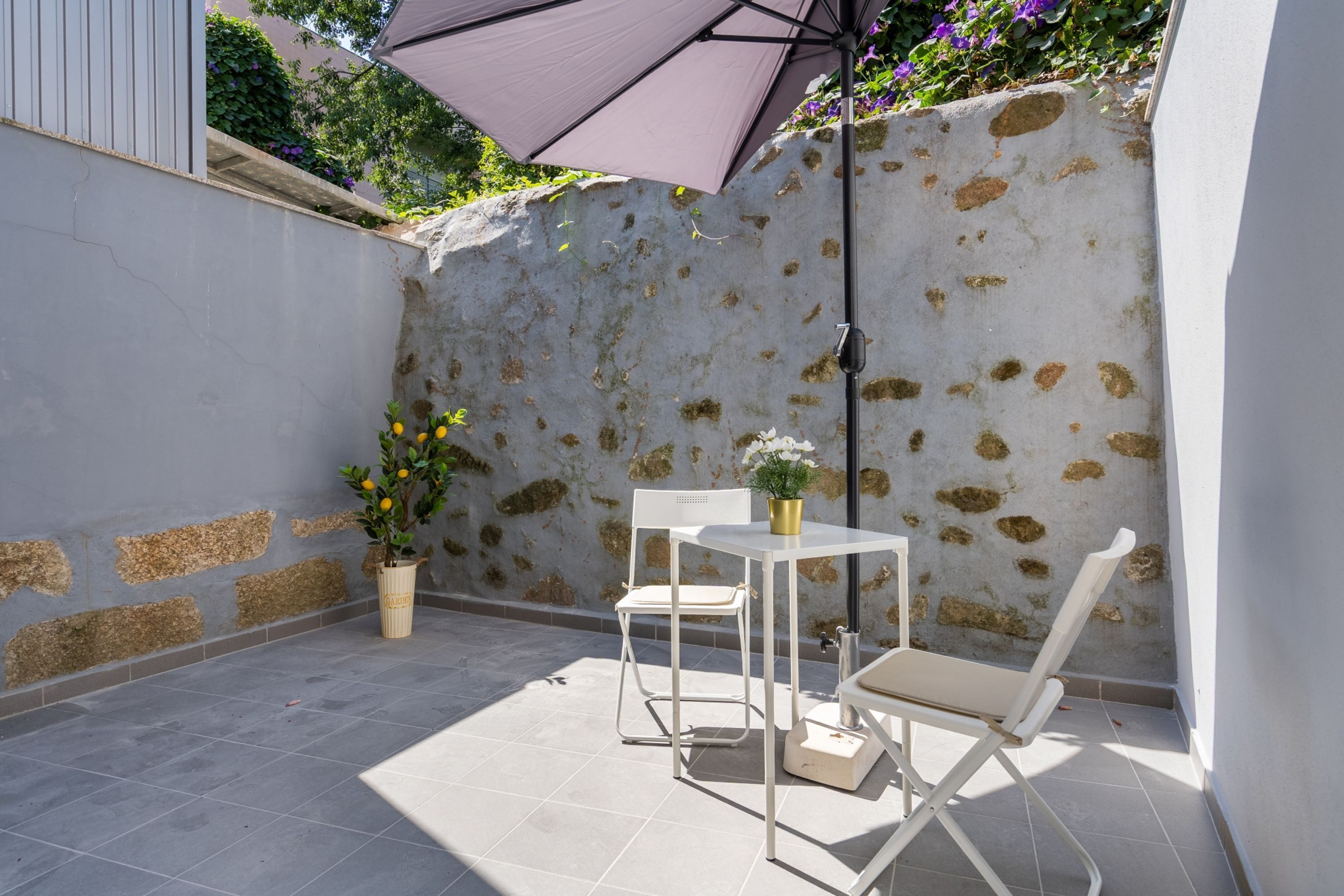 Une terrasse avec une table et des chaises blanches, une plante en pot et un parasol violet.