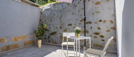 Une terrasse avec une table et des chaises blanches, une plante en pot et un parasol violet.
