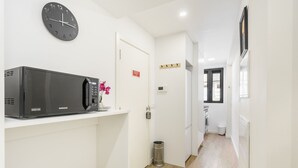 A hallway with a microwave on a shelf, a clock on the wall, a door with a sign, a trash can, and a window. - The Archway Studio by Minho s Guest (Braga)