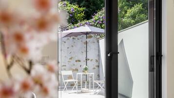 An outdoor seating area with white chairs and a table, a potted plant, and a purple umbrella.