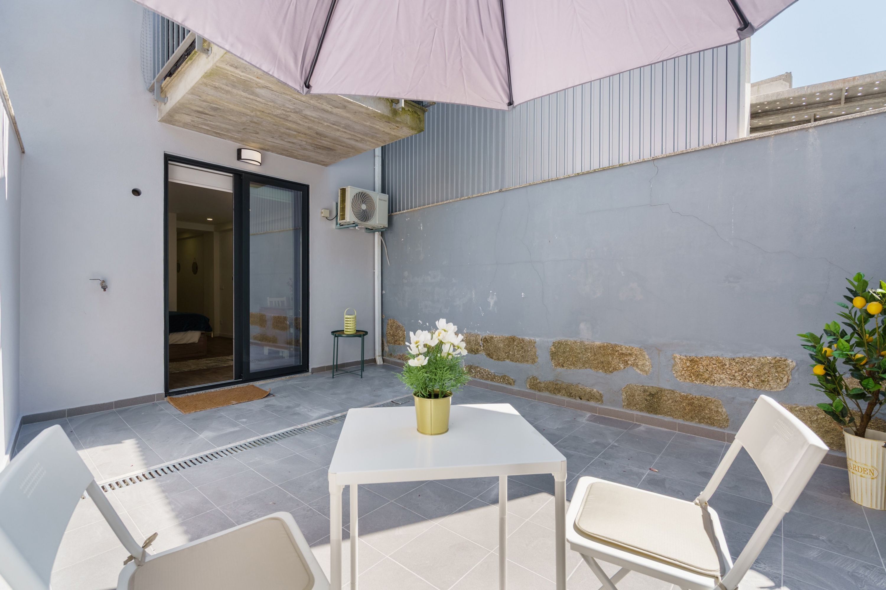 Une terrasse extérieure avec une table et des chaises, un pot de fleurs et une porte donnant sur une pièce.