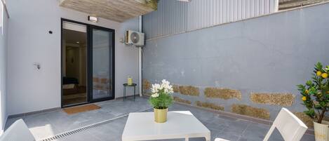 Une terrasse extérieure avec une table et des chaises, un pot de fleurs et une porte donnant sur une pièce.