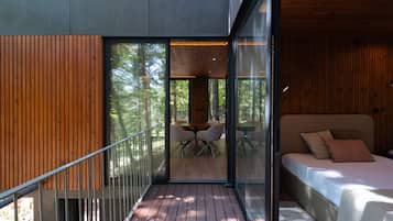 A modern interior with a wooden deck, a glass door leading to an outdoor seating area, and a bed with pillows.