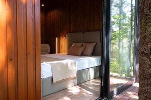 A bedroom with a bed, pillows, and a view of a forest through a glass door. - Prendal Eco Living Villa IV by Minho s Guest (Fafe)