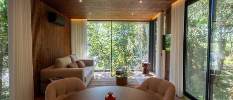 A modern interior with a wooden ceiling, large windows, a round table, and a sofa.
