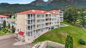 Un hotel de varios pisos con balcones, un estacionamiento y montañas al fondo.