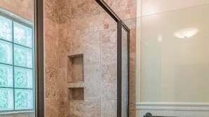 Une douche avec une porte en verre, un mur carrelé et une fenêtre ornée d’un motif décoratif.