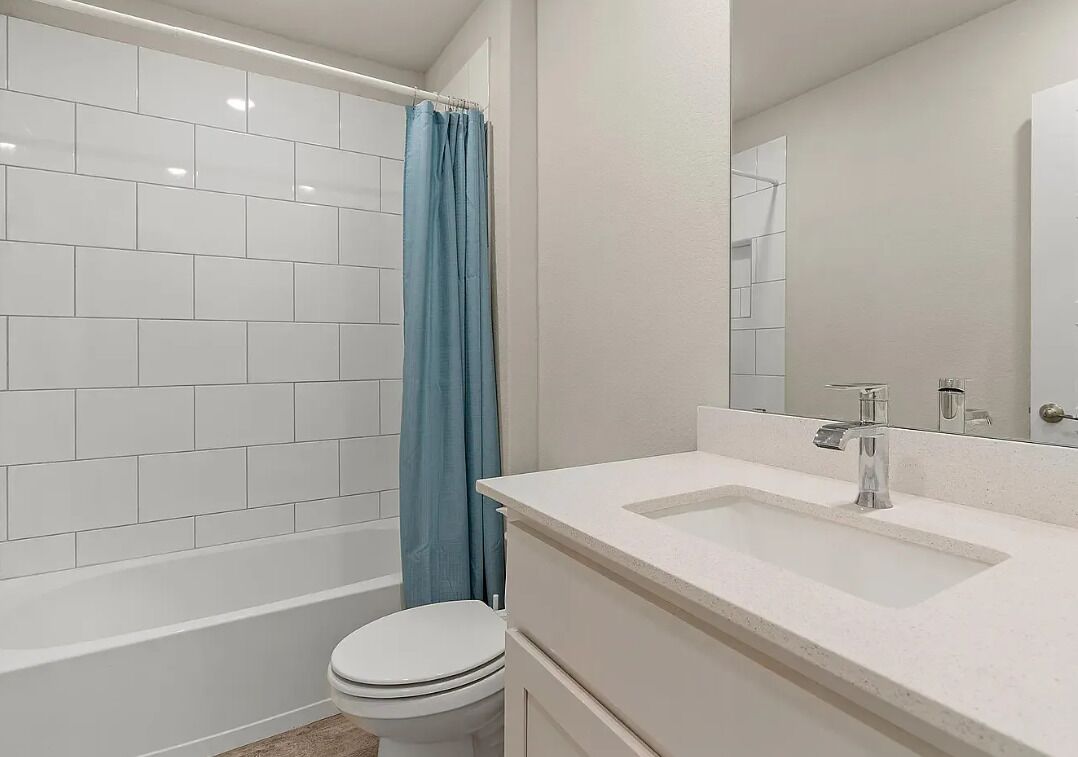 Une salle de bain avec une douche carrelée de carreaux blancs, un rideau de douche bleu, des toilettes blanches et un lavabo blanc avec un miroir au-dessus.