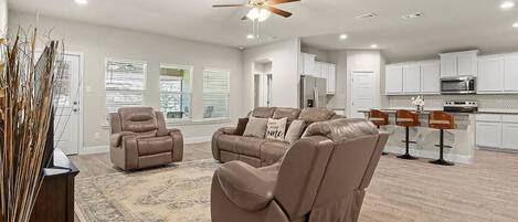 A spacious living area with a brown leather sofa, a recliner, and a ceiling fan.
