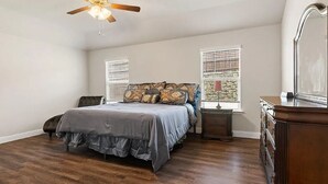 Un dormitorio con cama, ventilador de techo, cómoda y ventana con persianas.