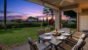 An outdoor patio with a table set for dining, surrounded by chairs, and a ceiling fan overhead. - Waikoloa Fairways #a101: Golf Course Ocean Views! (Waikoloa)