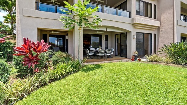 A multi-story building with a covered patio, outdoor seating, and a well-maintained garden. - Waikoloa Fairways #a101: Golf Course Ocean Views! (Waikoloa)