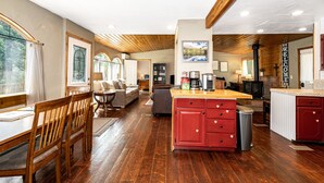 A spacious kitchen with wooden flooring, a central island, and a dining area with a wooden table and chairs. - Glacier Gateway Lodge | Hot Tub & Firepit (Hungry Horse)