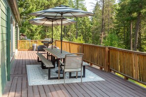 A wooden deck with picnic tables and umbrellas, surrounded by a wooden fence and dense trees.