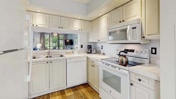 A modern kitchen with white cabinetry, a microwave, an oven, and a kettle. - Ground-floor condo with lagoon view, lanai, 2 pools, tennis, pickleball (Bradenton)
