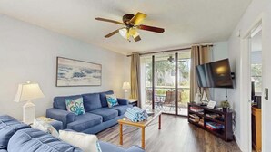 A living room with a sofa, a coffee table, a TV, and a ceiling fan. - Ground-floor condo with lagoon view, lanai, 2 pools, tennis, pickleball (Bradenton)