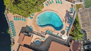 An aerial view of a resort with a central swimming pool, sun loungers, and a tennis court. - Ground-floor condo with lagoon view, lanai, 2 pools, tennis, pickleball (Bradenton)