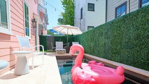 Una piscina con un flotador de flamenco rosa, sillas blancas y una mesa.