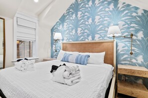 A hotel room with a large bed, a nightstand, a lamp, and a wall with a tropical leaf pattern. - Private Pool - 1 Block to King St - 4 Bedrooms (Charleston)