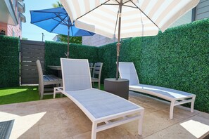 A patio with two lounge chairs, a striped umbrella, and a hedge wall. - Private Pool - 1 Block to King St - 4 Bedrooms (Charleston)