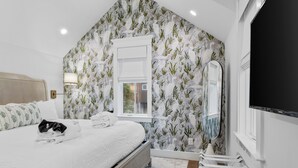 Un dormitorio con cama, ventana, televisión montada en la pared y un perchero.